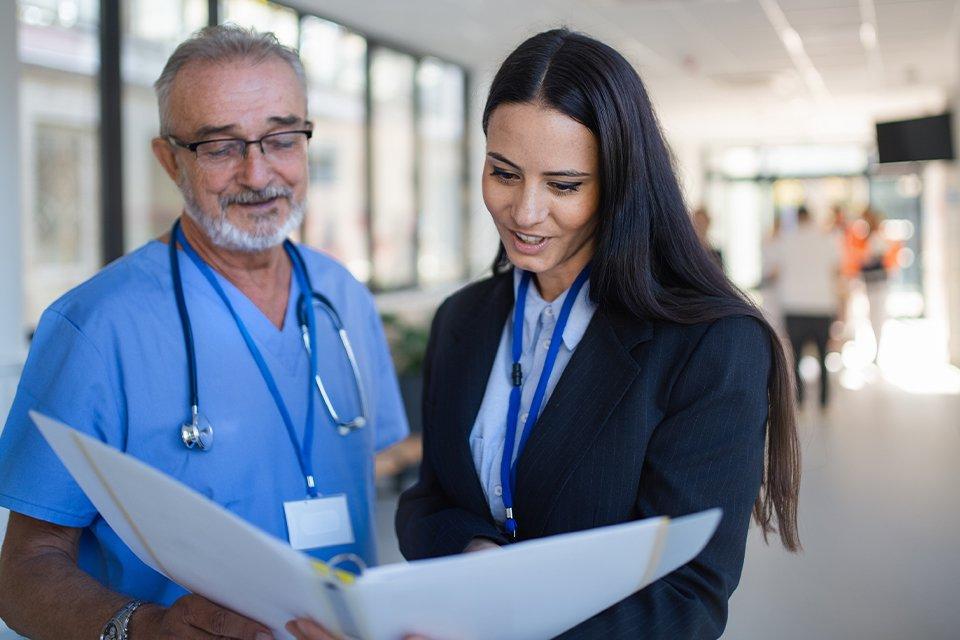 Healthcare administrator review files with a provider in the hallway of a healthcare facility.     